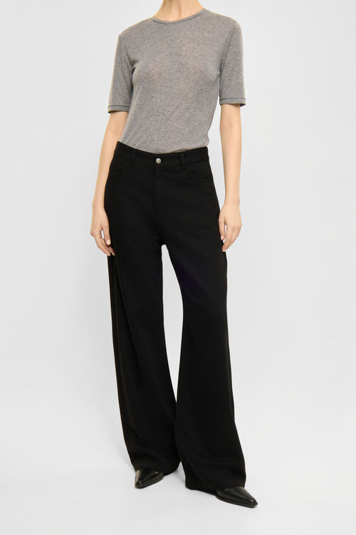 A model wearing a short-sleeve gray knit top and black wide-leg trousers, standing against a light gray studio background.